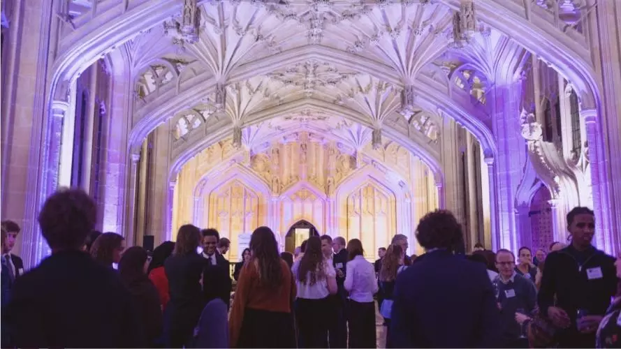 Picture of a crowd of guests inside the Divinity School, bathed in purple light