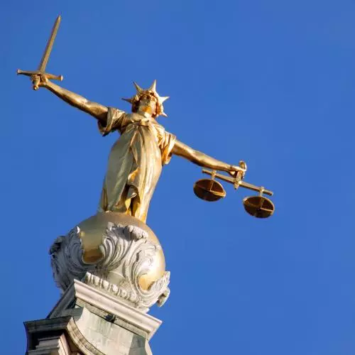 A picture of Lady Justice, a gold figure with arms outstretched holding a sword in one hand and scales in the other, against a clear blue sky